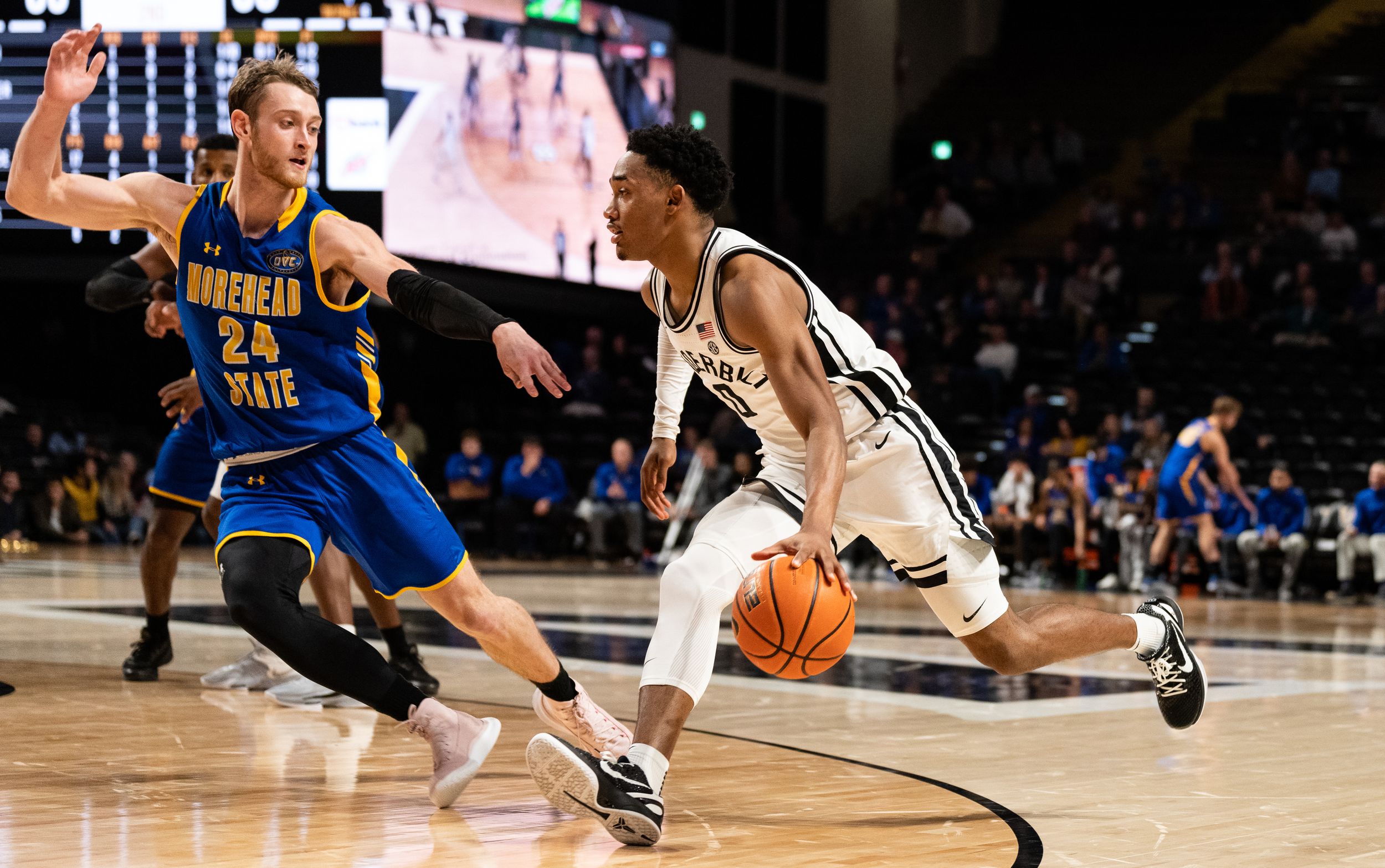 College basketball player drives past a Morehead State defender during an indoor arena game.