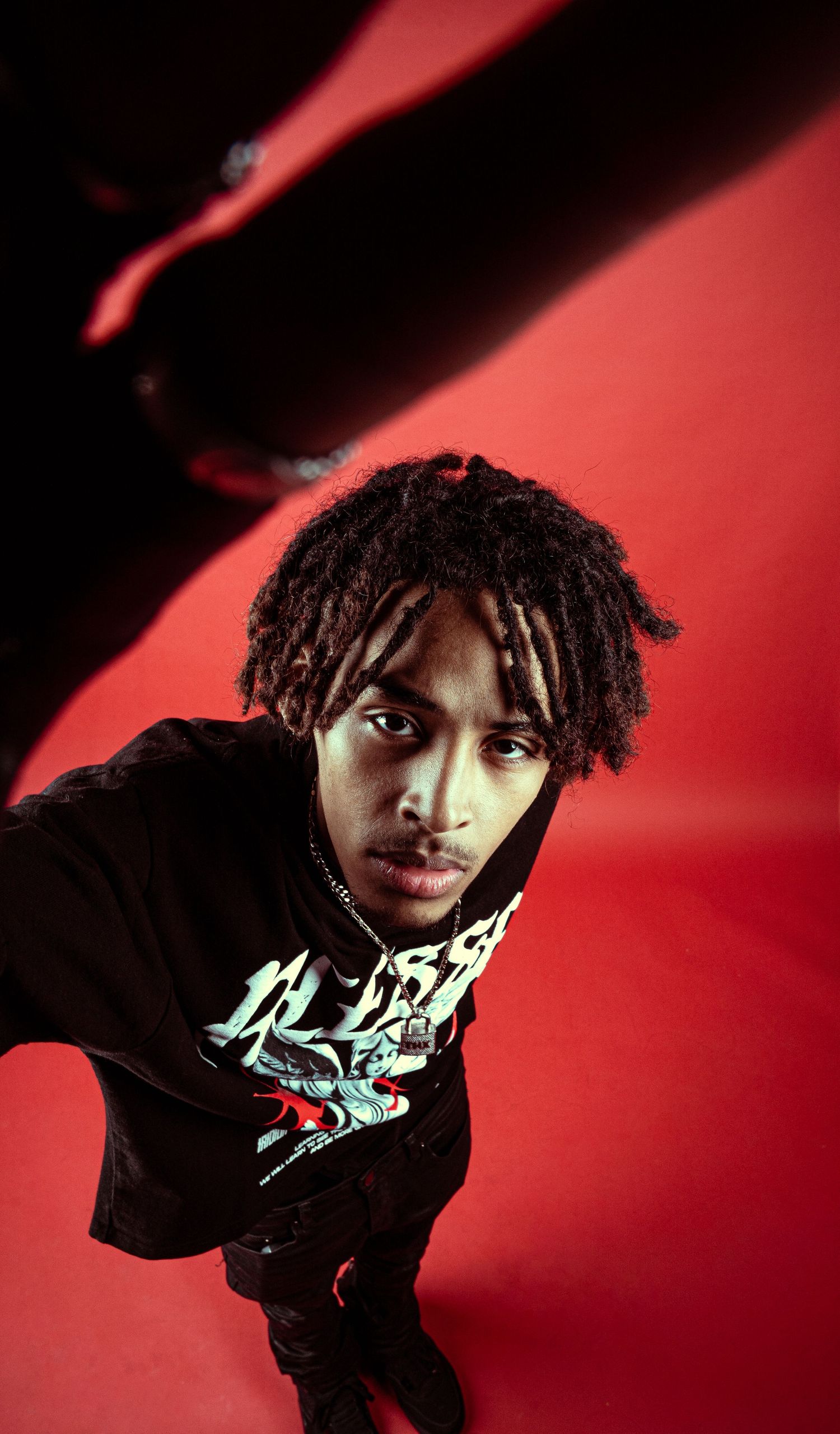 Artistic portrait against a red background showing someone in a black t-shirt shot from below.