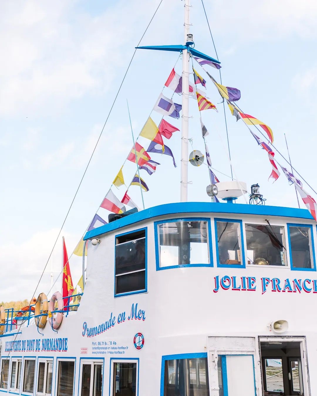 White passenger ferry decorated with colourful flags docked at a French harbour.