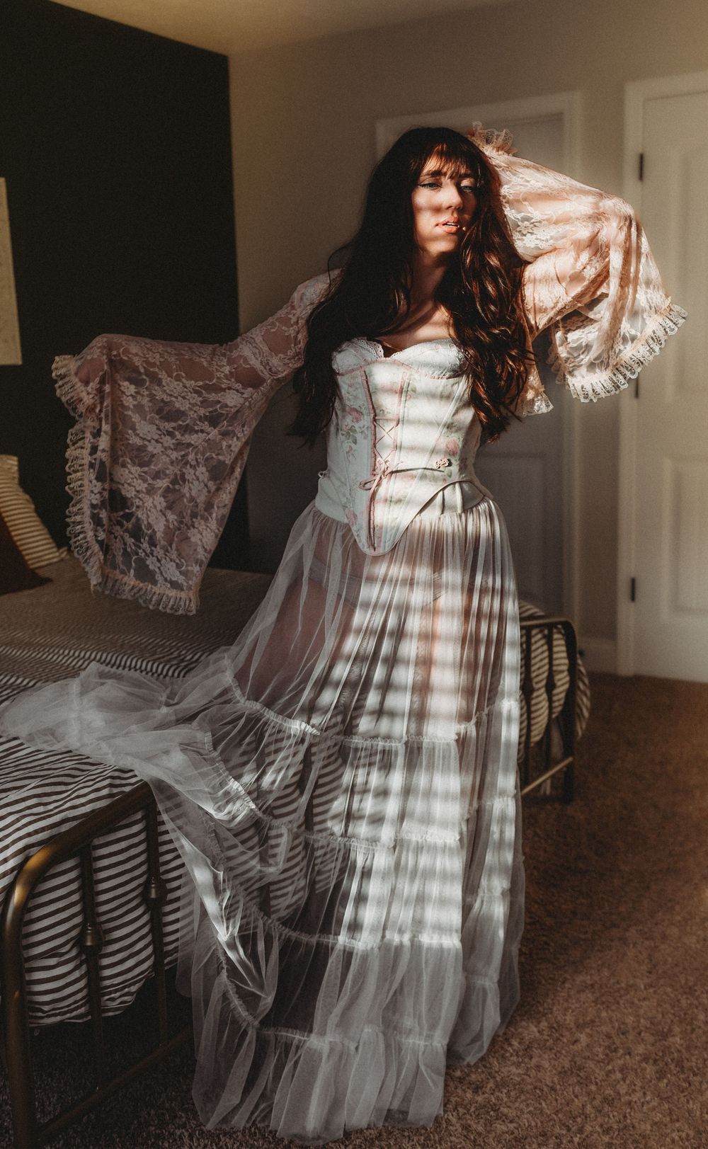 Delicate lace details and flowing fabric create a dreamy silhouette against a bedroom backdrop with natural light.