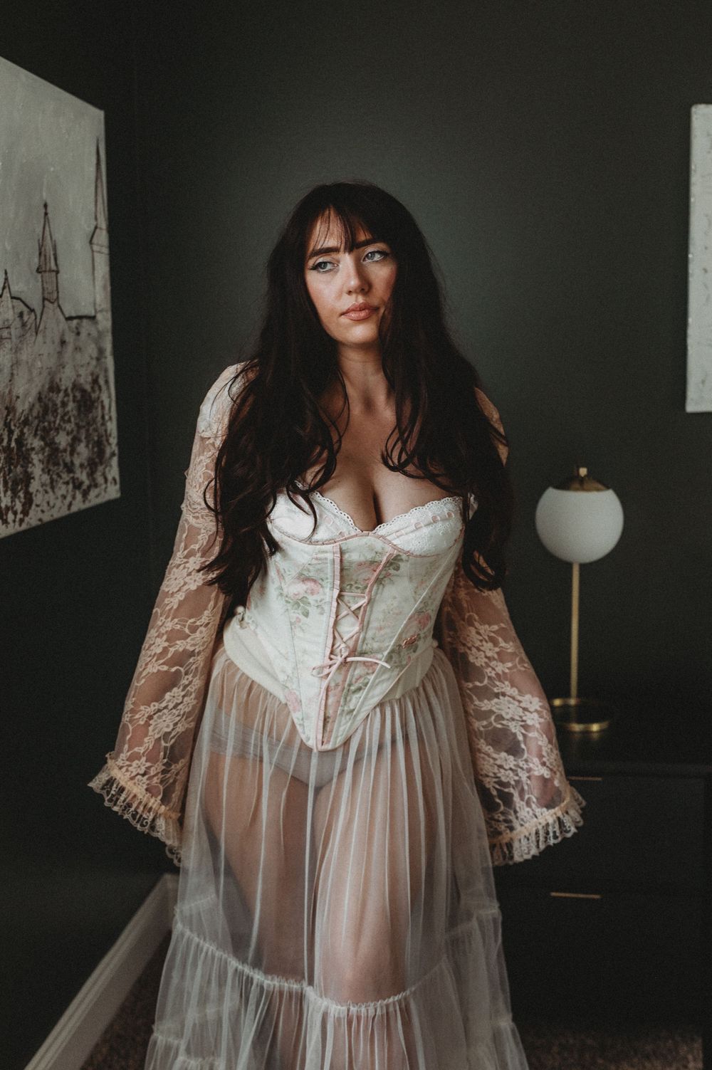 A moody boudoir photoshoot featuring a sheer white vintage-style nightgown against a dark background.