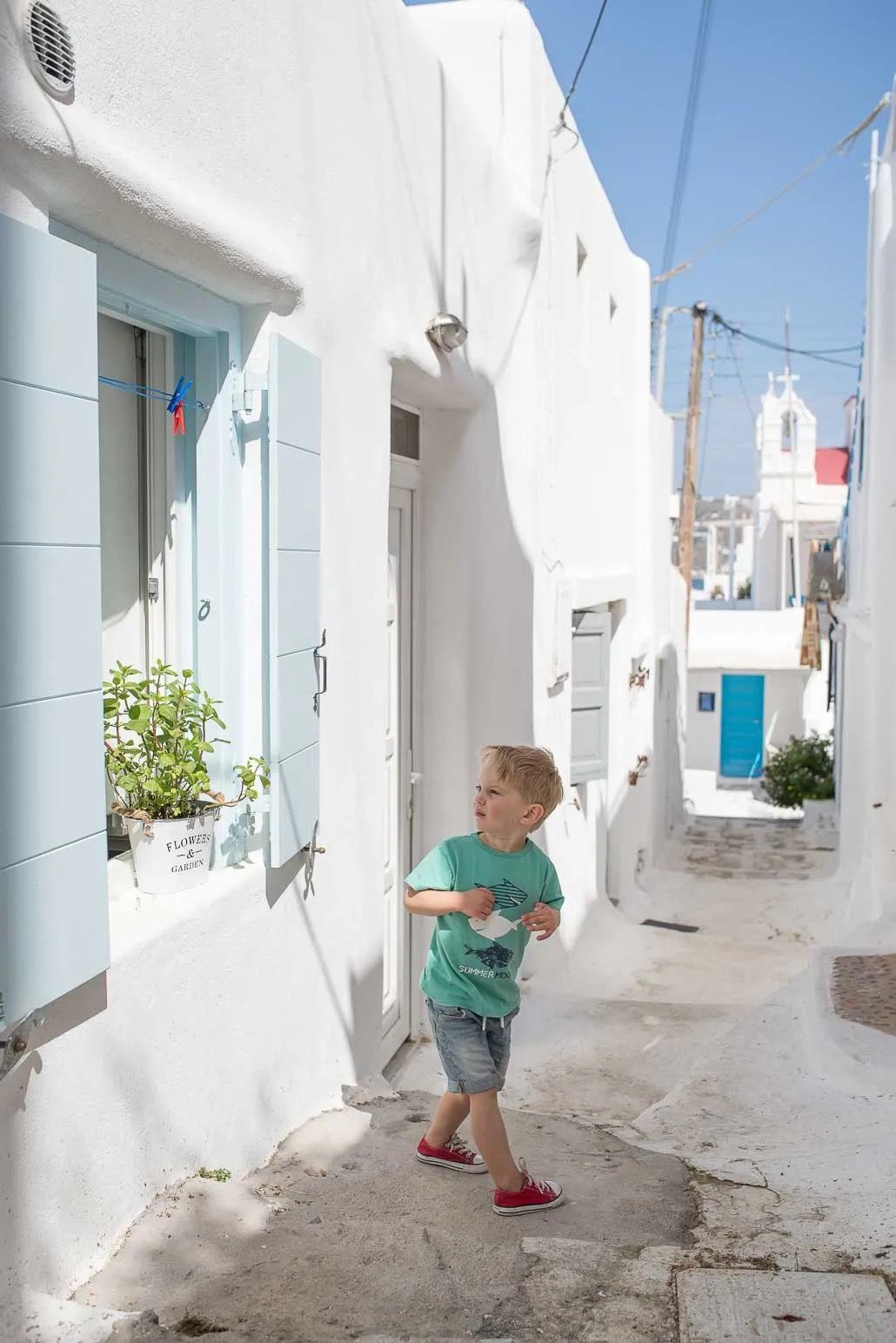 A narrow whitewashed alleyway in a Mediterranean village with blue accents and traditional architecture.