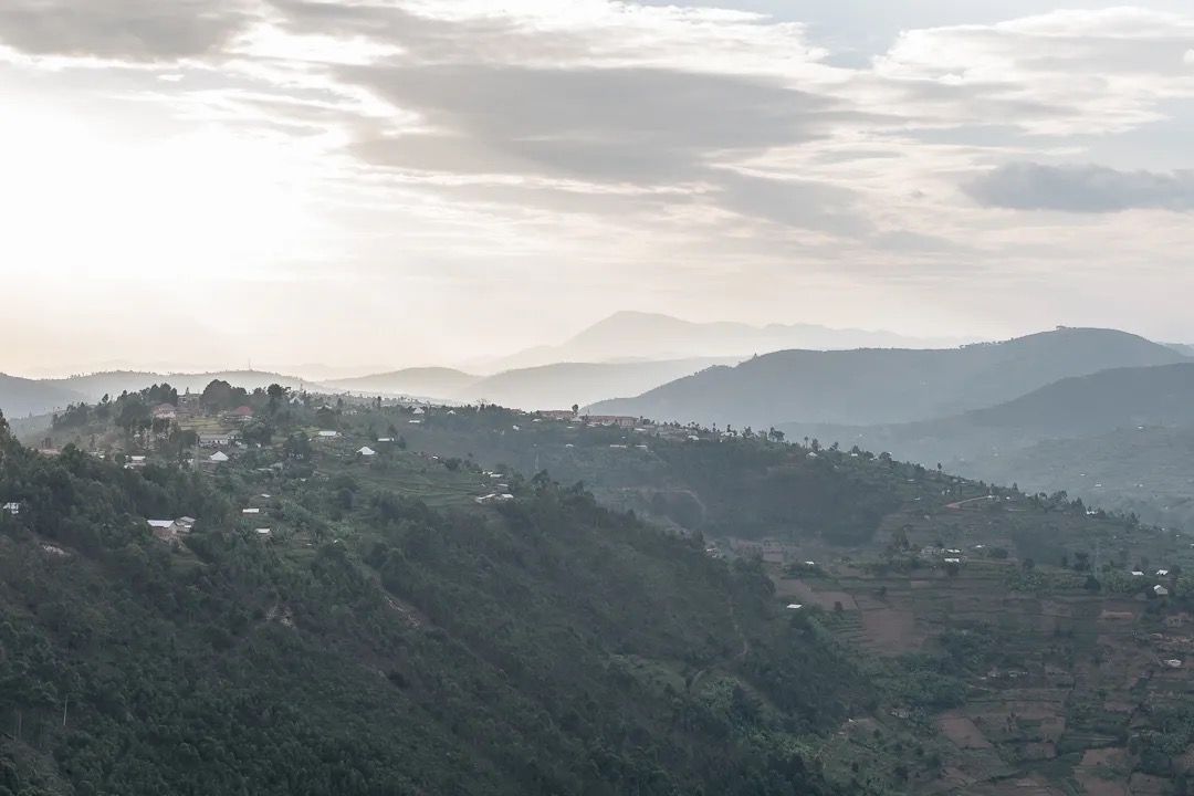 Soft morning light falls over rolling green hills and distant homes, showing peaceful highland scenery and rural landscapes.