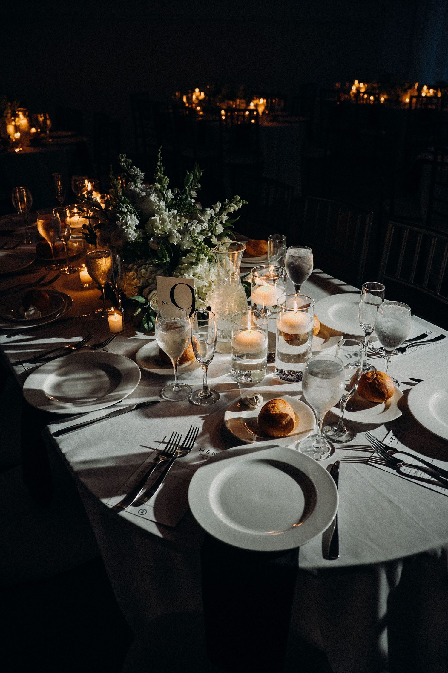 Elegant table settings with white plates, glowing candles, and floral centerpieces create an intimate dining atmosphere.