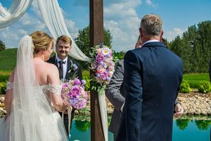 Outdoor wedding ceremony setup with white drapes and floral arrangements by a serene pond.