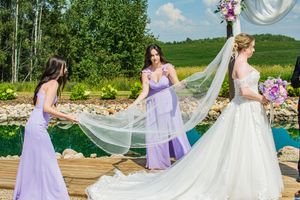 Wedding party in purple and white attire posing outdoors with flowing veil.