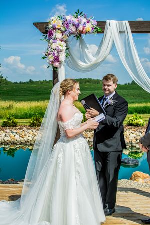 Wedding ceremony at a waterfront venue with floral arch and flowing white fabric decor.