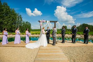 A panoramic view of an outdoor wedding ceremony setup with white chairs and floral arrangements by a serene pond.