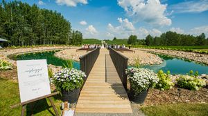 Long wooden bridge walkway decorated with white flowers leading to outdoor wedding venue.