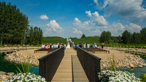 Aerial view of wedding ceremony setup on wooden bridge over water with guests seated.