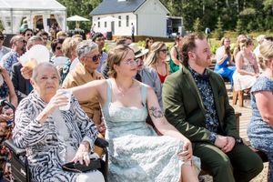 Wedding guests seated in rows outdoors watching ceremony under summer sky.
