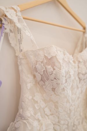 Close-up detail of a delicate white lace wedding dress bodice on a wooden hanger.