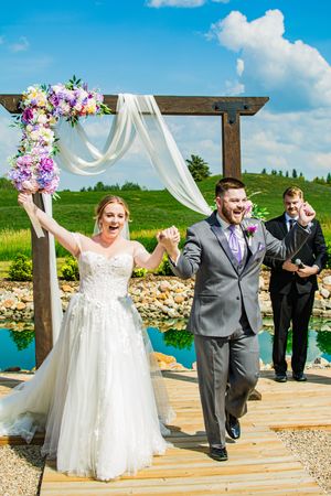 Newlyweds celebrate joyfully while walking down the aisle after their outdoor ceremony.