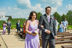 Wedding guests walk down an aisle lined with wooden benches at an outdoor venue.