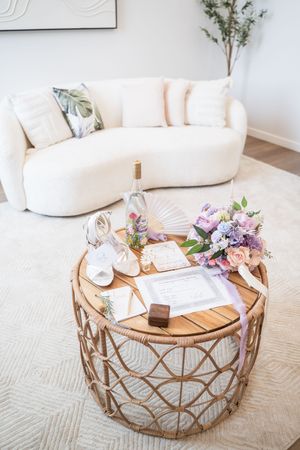Styled coffee table vignette with white sofa, wooden round table, and purple floral arrangement in modern living room.
