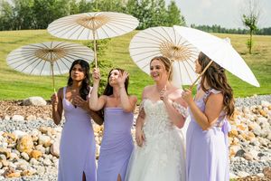Wedding party holding decorative white parasols poses together outdoors.