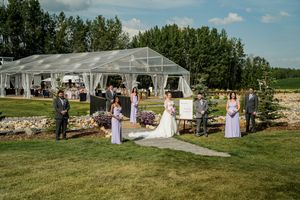 Outdoor wedding ceremony taking place under a clear tent structure with guests gathered on a landscaped lawn.