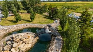 Panoramic view of a rustic outdoor wedding venue with a pond and lush greenery on a sunny day.