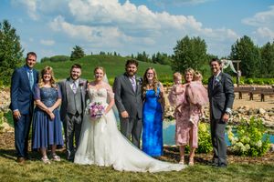 Wedding party poses for a group photo on a sunny day with landscaped gardens in the background.