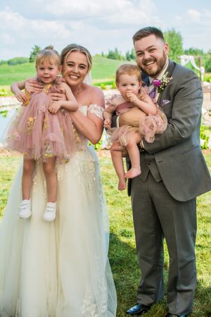 Wedding party poses playfully with a young child in pink tulle dress outdoors.
