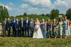 Large wedding party group photo outdoors with scenic landscape background.