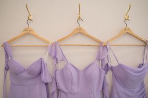 Several lavender and lilac bridesmaid dresses hanging on wooden hangers in a row.