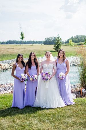 Bridal party in purple dresses poses by a lakeside with colorful bouquets.
