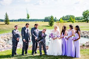 Wedding party posing together on a grassy field with mountains in the background.