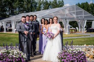 Wedding ceremony setup with clear tent, purple floral arrangements, and white chairs on manicured lawn.