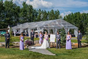 Panoramic view of an outdoor wedding ceremony setup with white tent and purple floral decorations.