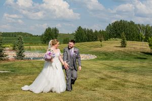 Couple in formal attire walking together across a scenic golf course landscape on their wedding day.