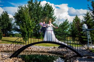 Couple posing on decorative arched bridge over pond in scenic wedding venue.