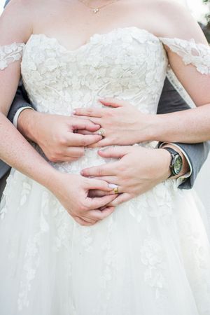 Detail shots of lace wedding dress bodice with hands showing engagement ring.