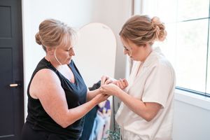 Two women share a tender moment during wedding preparations as they help each other get ready.
