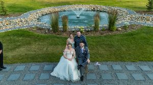 Aerial view of couple standing on stone patio with decorative pond and fountain in background.