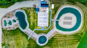 Aerial view of a waterpark complex with multiple pools, buildings, and landscaping surrounded by green areas.