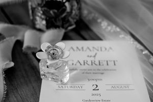 Black and white photo of a perfume bottle with floral detail resting on a wedding invitation.