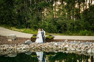A panoramic view of a wedding couple walking along a stone wall pathway surrounded by lush greenery.