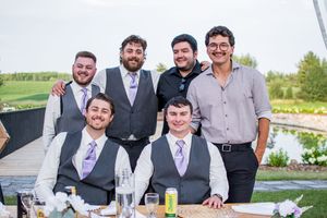 Groomsmen in grey suits and purple ties posing together at outdoor wedding.