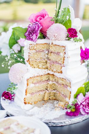 Elegant white wedding cake with pink and purple fresh flowers and exposed layers showing pink filling.