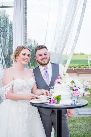 Wedding couple sharing cake at an outdoor reception with flowing white curtains and floral decorations.