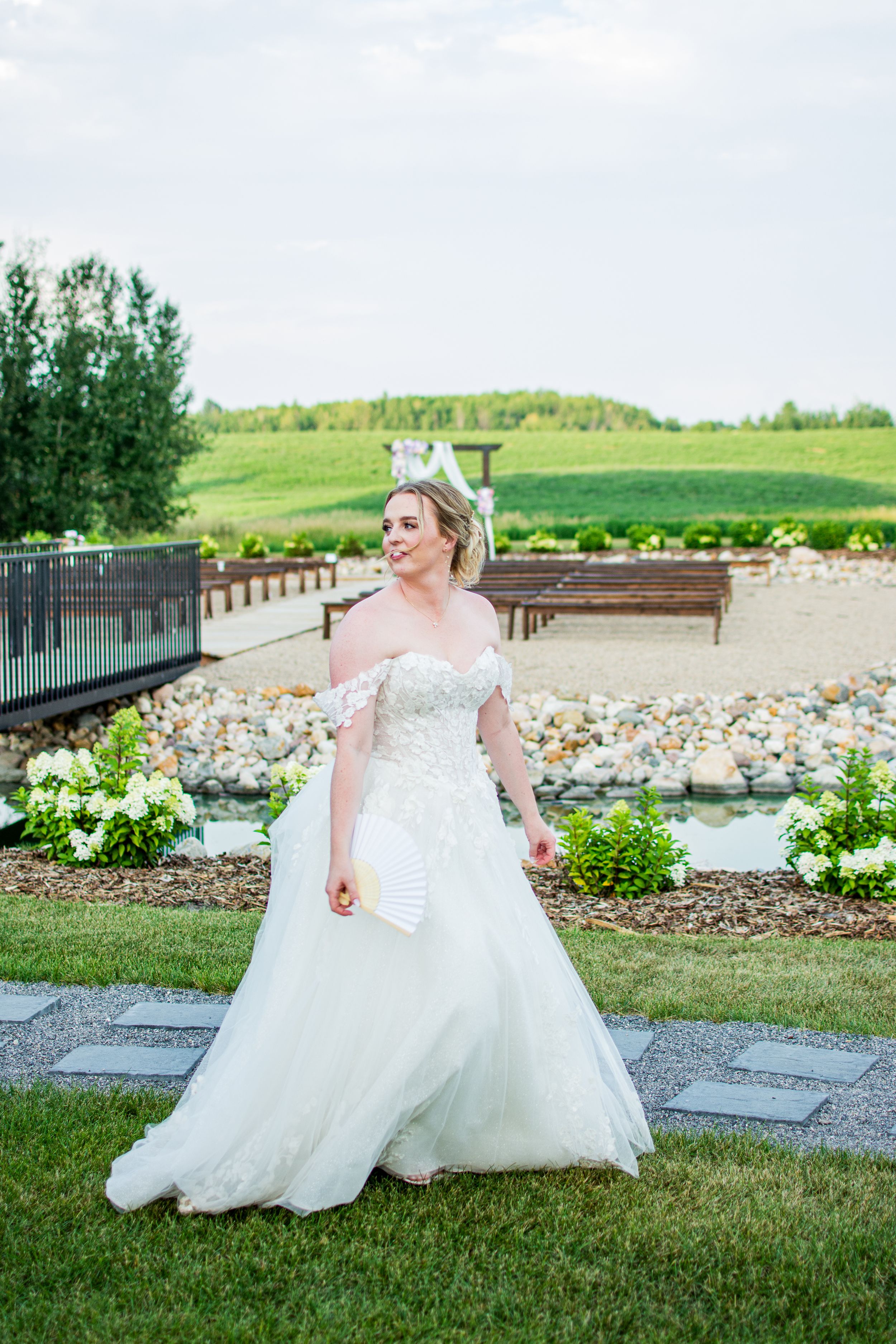 Bride in flowing white gown posing on landscaped garden grounds.