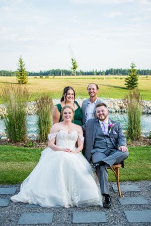 Wedding party relaxes on outdoor patio furniture with scenic pond view in background.