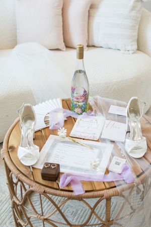 Round wooden coffee table decorated with wedding invitations, wine glasses and floral accents in a light-filled room.