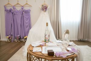 Purple bridesmaid dresses hanging on wooden hangers against a white wall with natural lighting.