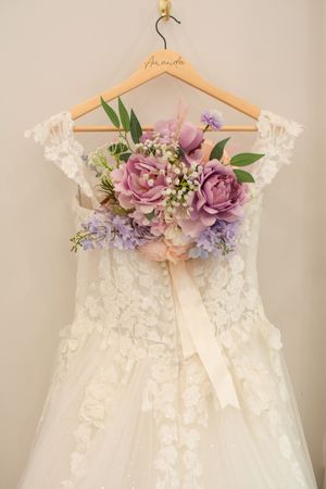 White lace flower girl dress on hanger decorated with pink and purple floral arrangements.