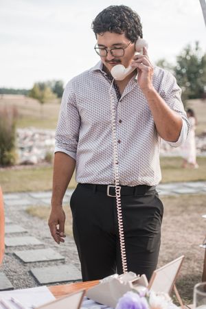 Close-up view of someone in glasses holding a vintage pink telephone at an outdoor event.