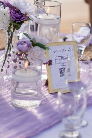 Elegant table setting with purple flowers, floating candles, and a QR code card for capturing photos.