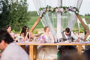 Outdoor wedding reception under white tent with floral decorations and table settings.