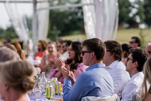 Outdoor wedding reception under white tent with guests seated at decorated tables.